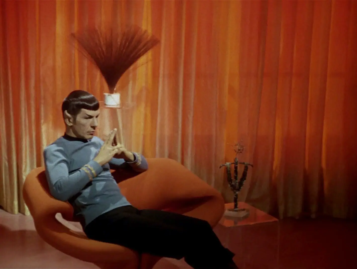 A screencap from Star Trek: The Original Series, depicting Spock sitting on an orange chair which resembles a folded ribbon.