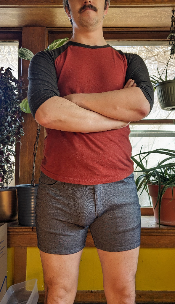 A man standing forward wearing a red shirt and gray shorts.