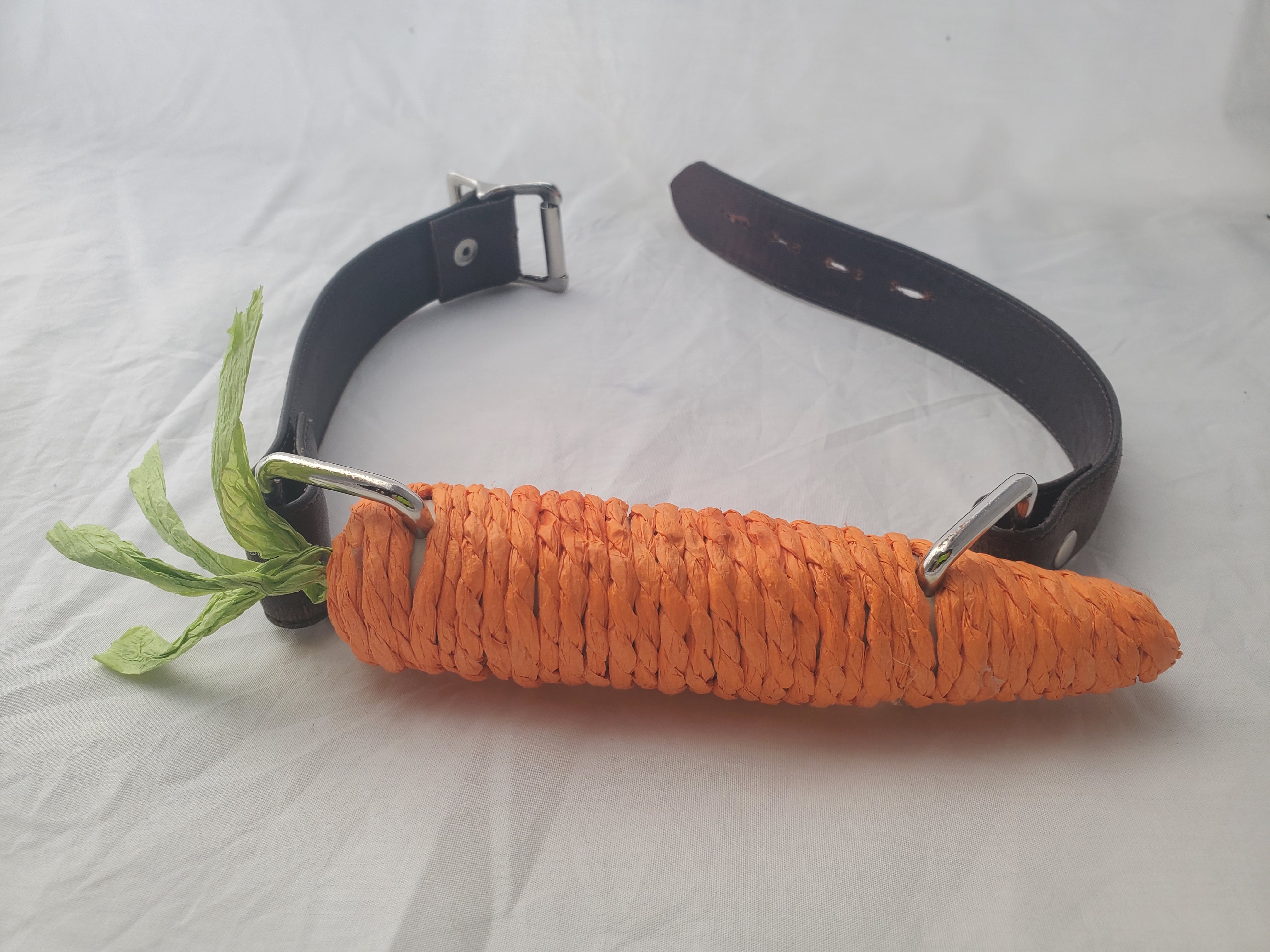 A carrot-shaped cat toy with buckled leather straps attched, turning it into a gag